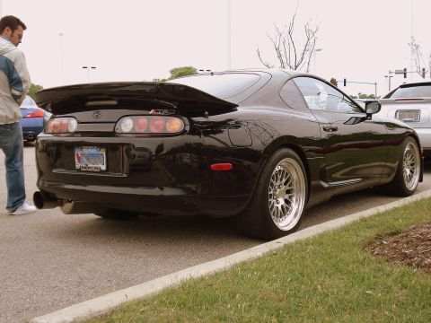 1998 Ford Taurus - A black Toyota Supra is parked on the side of the road, with a person standing nearby.