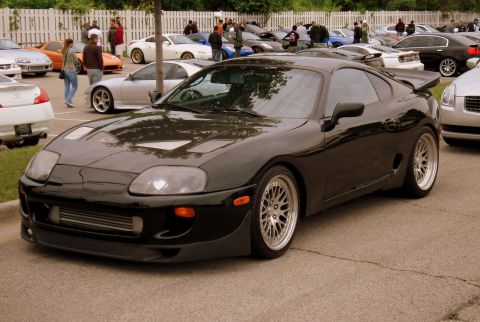 1998 Ford Taurus - A black sports car is parked at an outdoor car meet with other vehicles in the background.