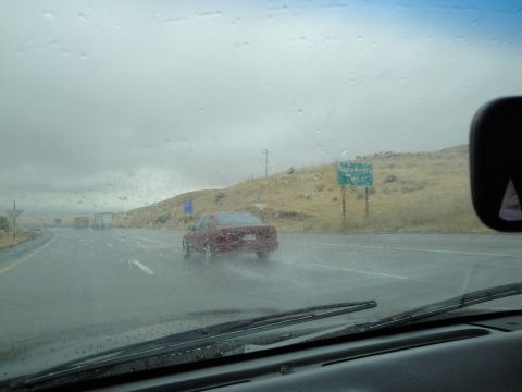 1990 Ford Taurus - Driving on a wet highway with a red sedan ahead and trucks in the distance.