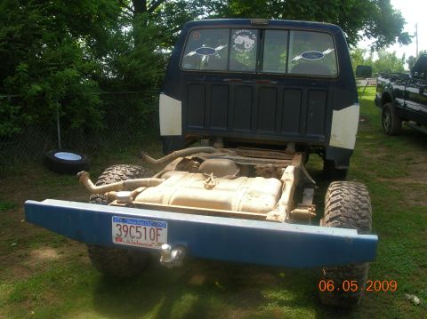 1991 Ford F-150 - The rear of a pickup truck, stripped down to its chassis, sits in a grassy yard with a fence and trees in the background.