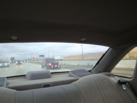 1990 Ford Taurus - A red sedan is seen driving on a highway with other vehicles under a cloudy sky.