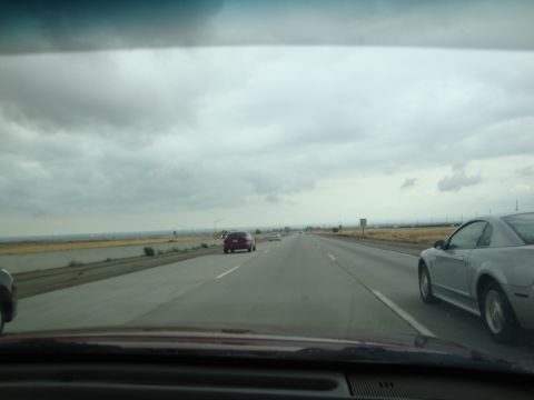 1990 Ford Taurus - A silver coupe is seen from the passenger side on a highway with other vehicles in the distance under a cloudy sky.