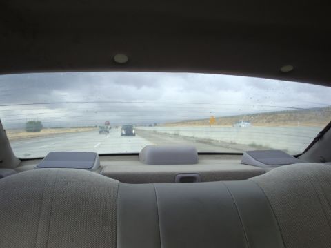 1990 Ford Taurus - Looking out the rear window at a highway with multiple vehicles under a cloudy sky.