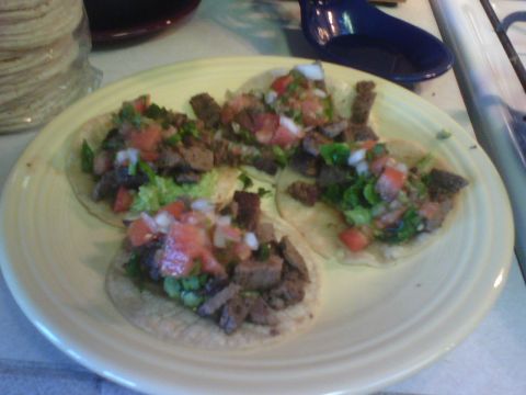 1984 Ford Bronco - A plate of three tacos, topped with chopped meat and pico de gallo, sits on a counter next to a stack of tortillas.