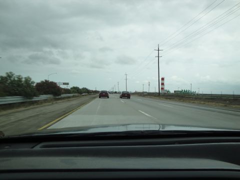 1990 Ford Taurus - Driving on a highway with two cars ahead and industrial structures in the distance.