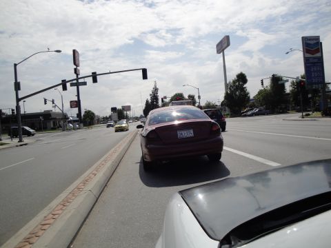 1990 Ford Taurus - A red sedan is seen from behind while driving on a street with a Chevron gas station in the background.