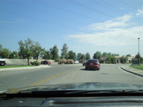 1990 Ford Taurus - A red sedan drives on a road with other vehicles and buildings in the background under a clear blue sky.