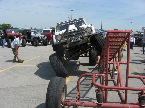 1987 Suzuki Samurai - A modified Suzuki Samurai is shown at an extreme angle on an obstacle, with other vehicles parked nearby.