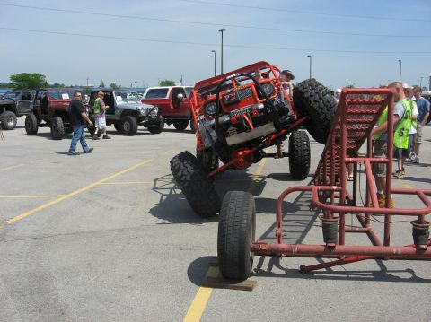 1987 Suzuki Samurai - An orange off-road buggy is tilted on its side, with other off-road vehicles and people visible in the background.