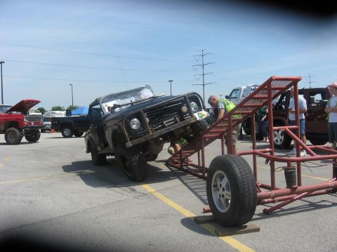 1987 Suzuki Samurai - A vehicle is positioned on an obstacle course ramp, with people observing.