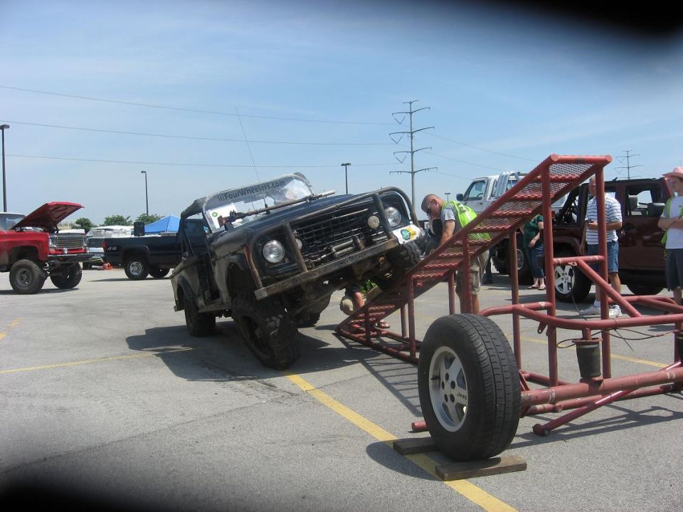 Off-road vehicle attempting an obstacle course, with other trucks parked nearby