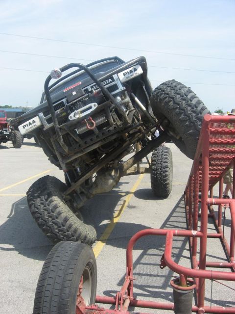 1987 Suzuki Samurai - A heavily modified off-road vehicle is positioned on a red metal obstacle, with "TOYOTA" visible on its front.