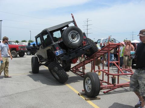 1987 Suzuki Samurai - Modified Jeep Wrangler attempting an obstacle on a ramp, with spectators and other vehicles present.