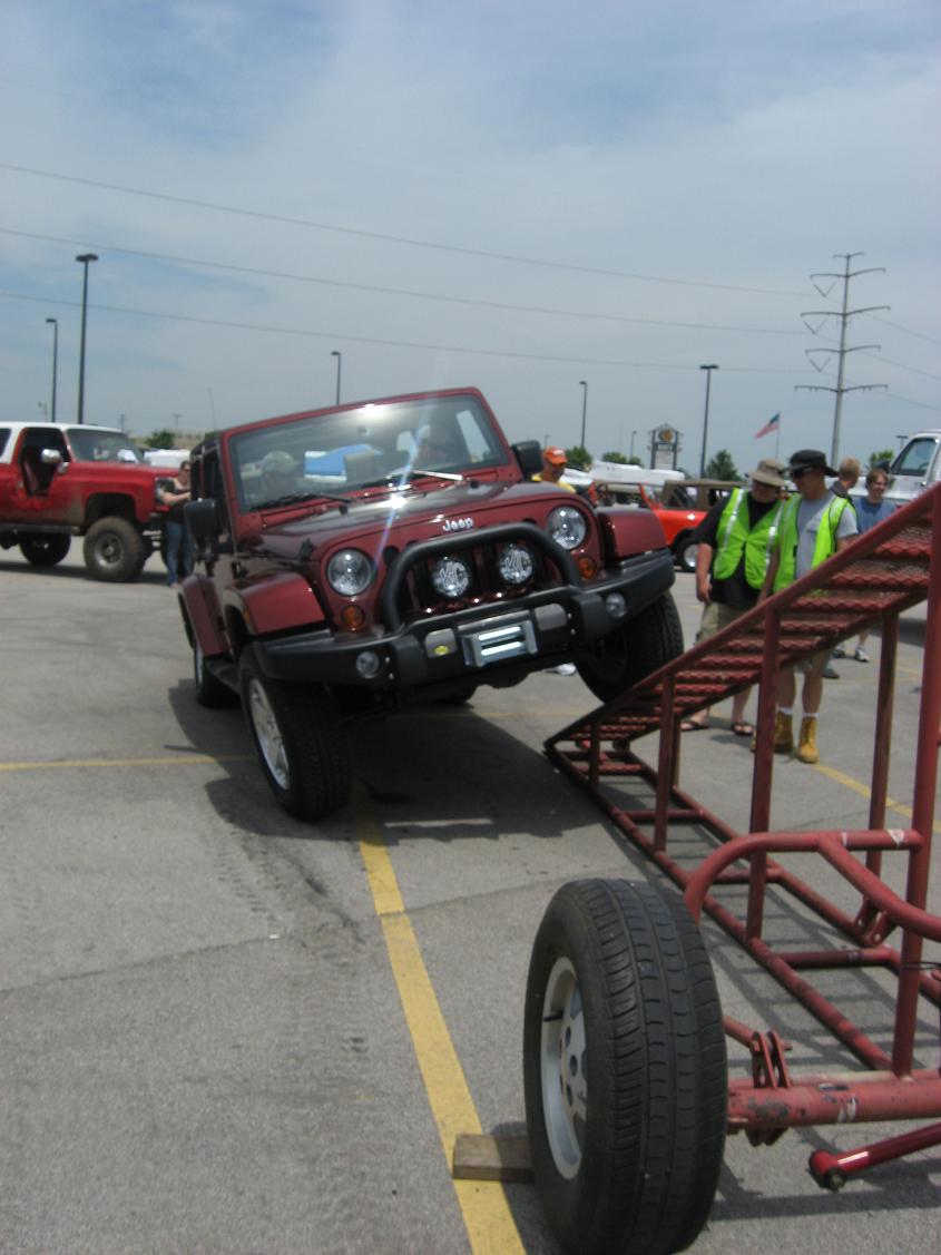 Red Jeep Wrangler on a metal ramp, front wheels elevated