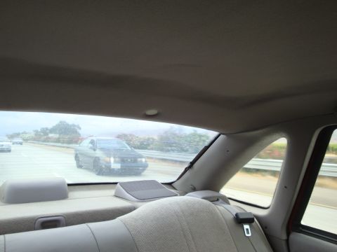 1990 Ford Taurus - A dark sedan is seen driving on the highway, viewed from the back seat of another vehicle.