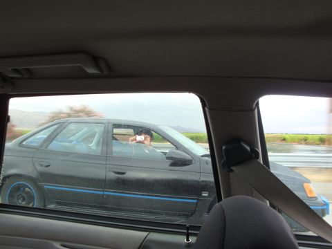 1990 Ford Taurus - A black sedan with blue trim drives down the highway, its driver taking a photo.