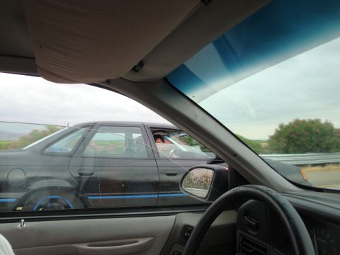 1990 Ford Taurus - A black 1990 Ford Taurus with distinctive blue trim is seen from inside another vehicle on a highway.