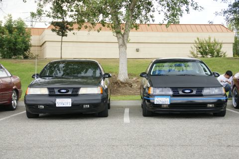 1990 Ford Taurus - Two 1990 Ford Taurus sedans are parked in a lot, one with a blue stripe on its grille.