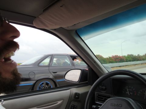 1990 Ford Taurus - A person's face is visible in the foreground, looking out the window at another car driving alongside on the highway.