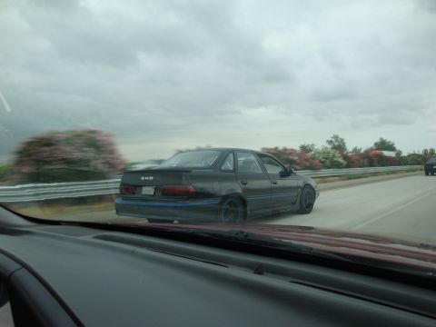 1990 Ford Taurus - A black 1990 Ford Taurus SHO with distinctive blue trim is seen from another vehicle on a highway.