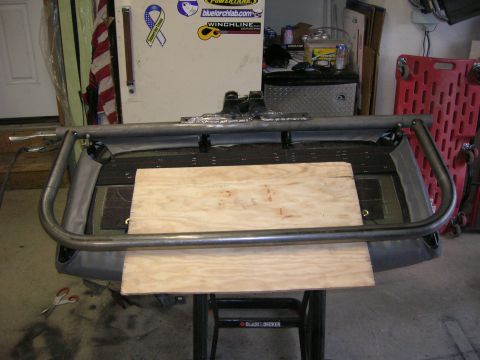 1996 Ford Bronco - A metal roll cage section is positioned over wooden planks, resting on a workbench in a garage setting.
