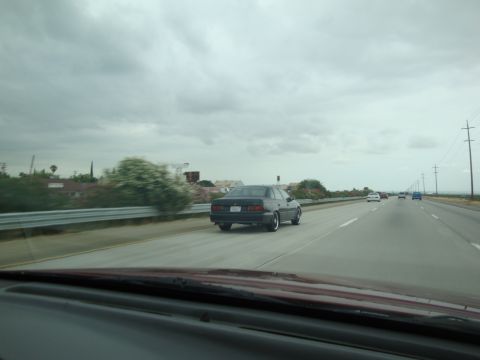 1990 Ford Taurus - A dark sedan is seen driving on a highway under a cloudy sky.