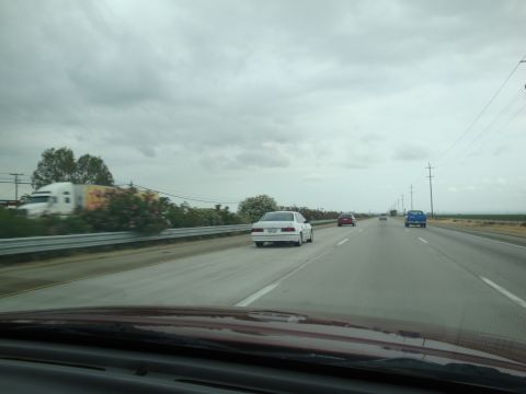 1990 Ford Taurus - A white 1990 Ford Taurus sedan travels down a highway on a cloudy day.