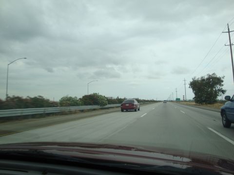 1990 Ford Taurus - A view from inside a vehicle driving on a highway under a cloudy sky.