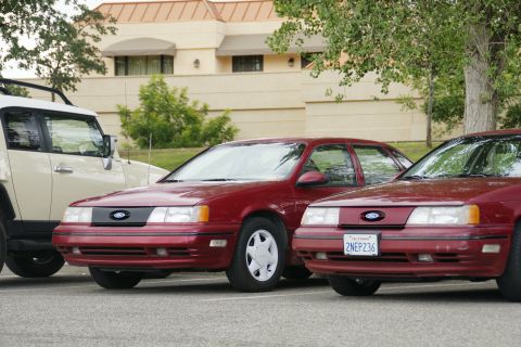 1990 Ford Taurus - Two Ford Taurus sedans are parked in a lot, with a white SUV on the left.