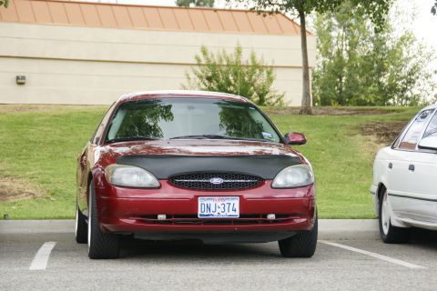 1990 Ford Taurus - Front view of a red Ford Taurus, parked next to another vehicle.