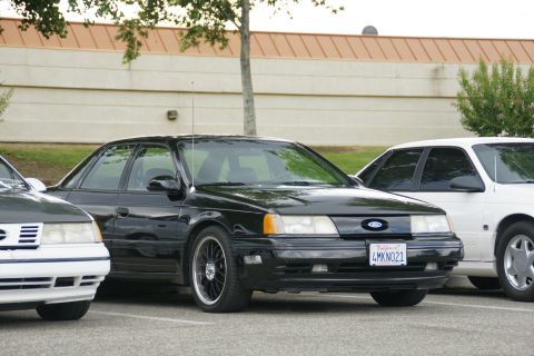 1990 Ford Taurus - Front view of a black 1990 Ford Taurus sedan, parked alongside other vehicles.