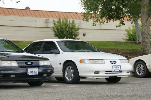 1990 Ford Taurus - Two Ford Tauruses are parked in a lot, with a third vehicle partially visible on the right.