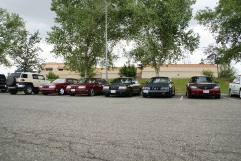 1990 Ford Taurus - Several cars are parked in an outdoor lot under a cloudy sky.