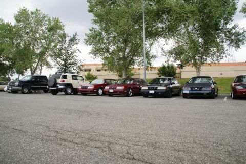 1990 Ford Taurus - A dark blue sedan is parked in a lot with several other vehicles visible.