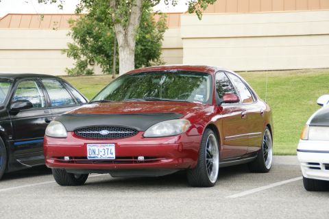 1990 Ford Taurus - Front view of a red Ford Taurus sedan with a black car bra and custom wheels.