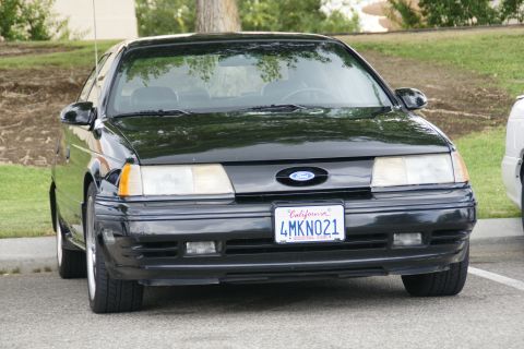 1990 Ford Taurus - A black 1990 Ford Taurus is parked outside on a sunny day.