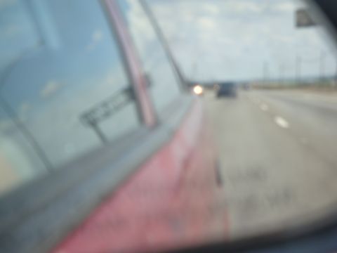 1990 Ford Taurus - View from a car's side mirror shows a highway with traffic and cloudy skies.