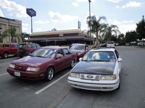 1990 Ford Taurus - Two Ford Taurus sedans, one maroon and one white with a black hood, parked outside a China Town Buffet.