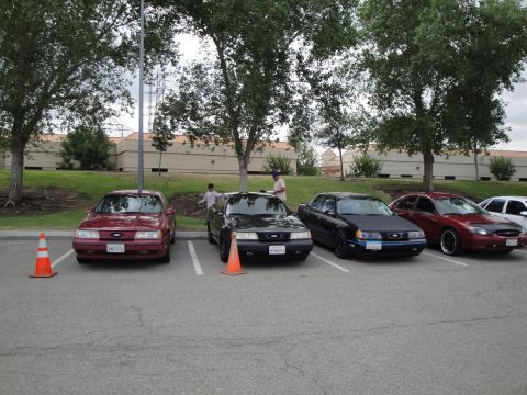 1990 Ford Taurus - A red 1990 Ford Taurus sedan is parked in a lot with other vehicles.