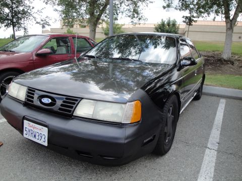 1990 Ford Taurus - 1990 Ford Taurus, front 3/4 view, parked in a lot with another car.