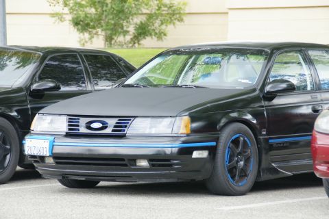 1990 Ford Taurus - A black 1990 Ford Taurus with custom blue accents is parked next to another vehicle.