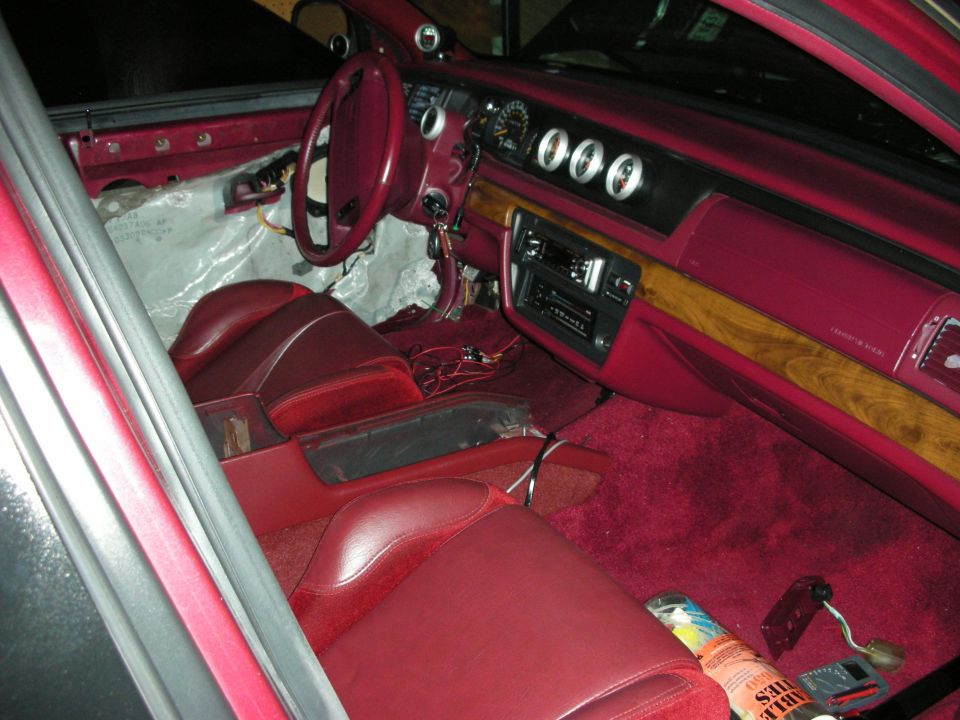 Red interior of a 1992 Ford Crown Victoria with aftermarket gauges and exposed wiring