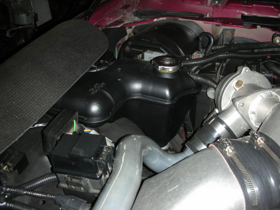 Close-up of a car's engine bay, showing the coolant reservoir and some piping