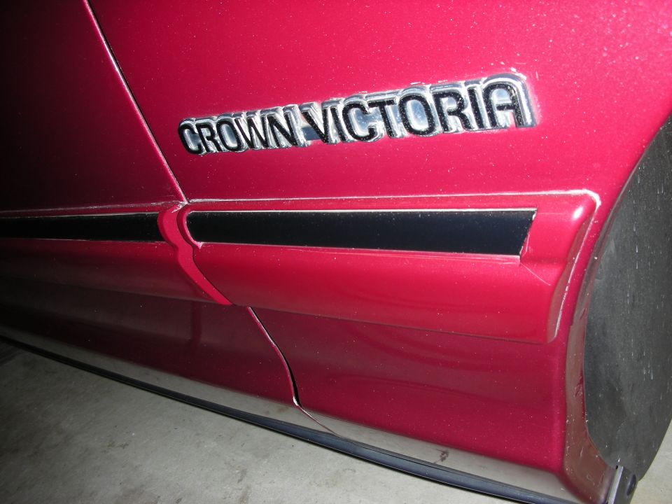 Close-up of a red car's side showing the 'CROWN VICTORIA' emblem