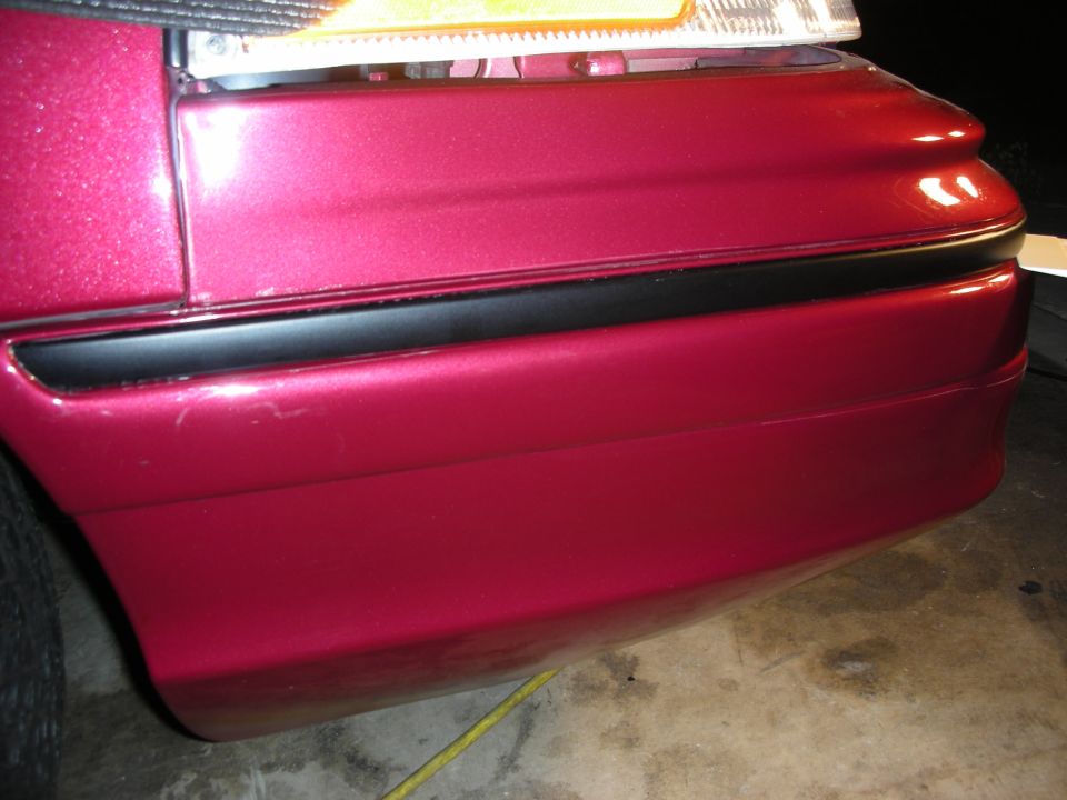 Red 1992 Ford Crown Victoria rear bumper and taillight, close-up side view. The paint has minor scuffs