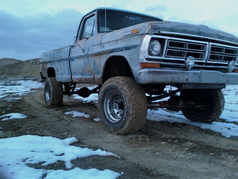 1971 Ford F-100 - This lifted pickup truck is parked on a muddy, snowy dirt road with hills in the background.