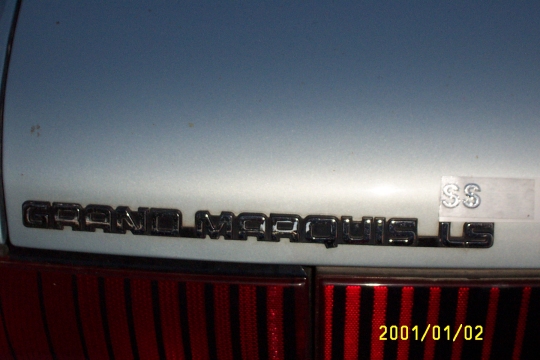 Close-up of GRAND MARQUIS LS trunk badge on light silver car with red taillights below