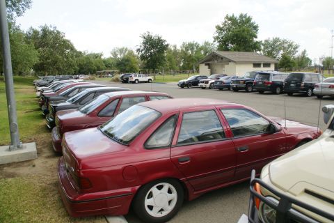 1990 Ford Taurus - A line of cars are parked in a lot, with a red sedan in the foreground.
