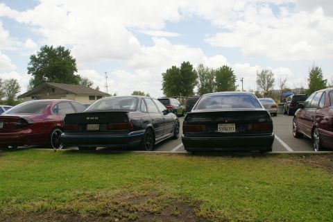 1990 Ford Taurus - Two black Ford Taurus SHO sedans are parked in a lot, with a red Taurus visible to the left.