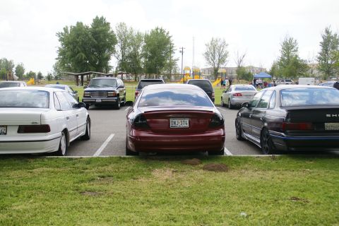 1990 Ford Taurus - Rear view of a red sedan with aftermarket taillights and a spoiler, parked in a lot with other vehicles.
